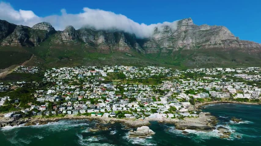 Luxury homes and rocky shorelines extend beneath a dramatic cloud-capped mountain range.
