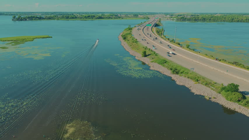 Drone perspective of U.S. Route 41 bridge spanning the Fox River waterways in Oshkosh, Wisconsin with a motorboat cruising near traffic on a sunny day.