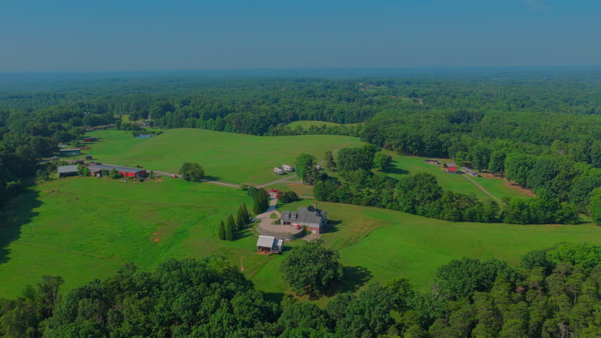 Near Pilot Mountain State Park, a brick country home with circular drive, outbuildings, red barns and mown pasture spread across rolling wooded acreage in the North Carolina Piedmont.