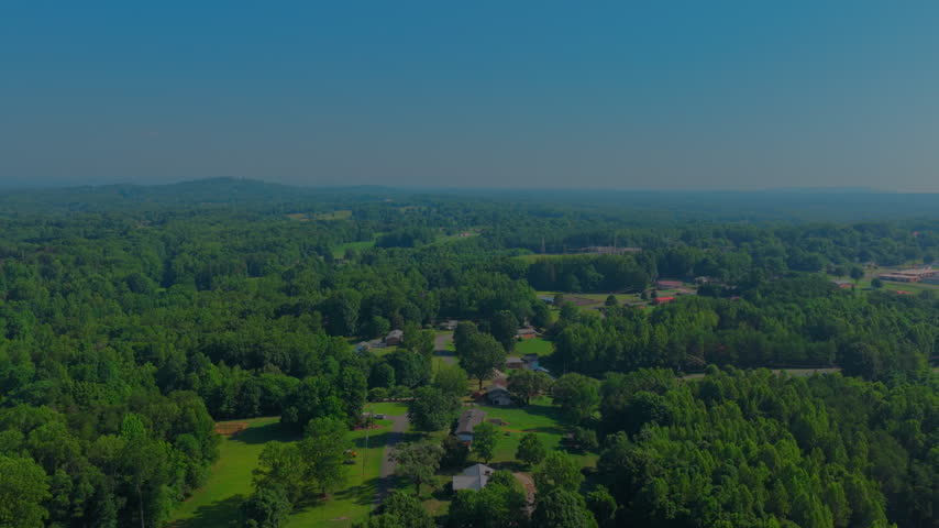 Rolling green pasture, hardwood forest and scattered farmsteads fade into hazy blue ridges — the characteristic summer landscape of the North Carolina Piedmont.
