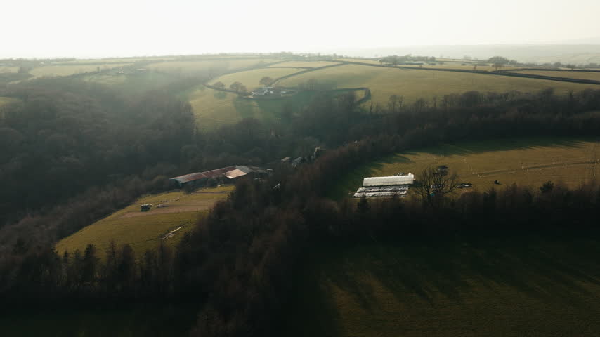 An aerial top-down view shows a farmhouse and outbuildings surrounded by trees in the rural landscape.