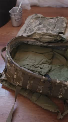 Soldier carefully folding military combat uniform and placing clothing inside pixel camouflage tactical backpack.