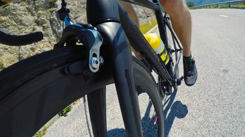 A cyclist rides a carbon road bike on a sunny mountain path, featuring a close-up of the bike