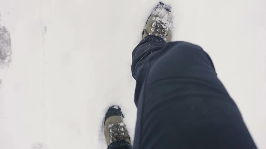 Person hiking through deep winter snow in mountains wearing dark trousers and boots capturing point of view steps across fresh white frozen terrain during cold seasonal day