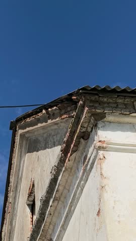 Barn swallow flying near old dilapidated building roof under blue sky