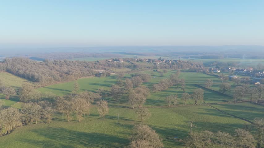 Drone footage capturing a panoramic aerial view of the rural countryside in Nievre, France. The video showcases a small French village surrounded by green fields, scattered farmhouses, agricultural
