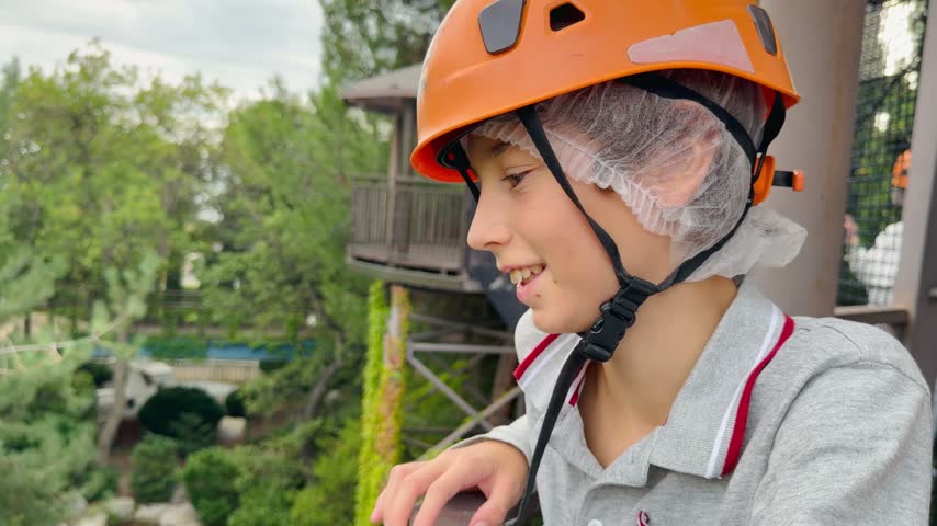  Kid in orange safety helmet on rope park zipline platform — side close-up