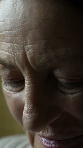 Extreme close-up of a person wearing transparent rectangular eyeglasses, with one eye visible through the lens and a hand touching the frame near the temple.