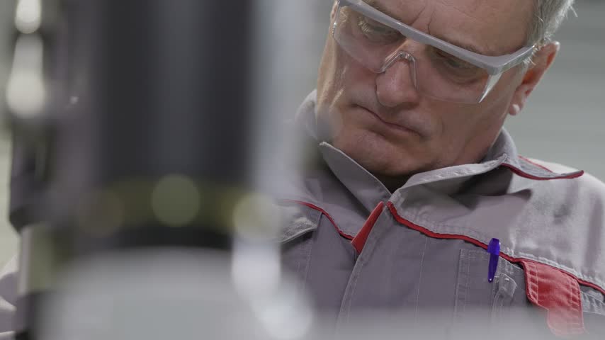 Portrait of an adult male technician in protective glasses and overalls, who works at a factory with machine tools.