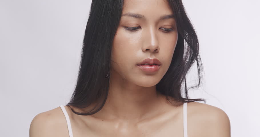 Close up portrait of beautiful Asian woman smiling with glowing clear skin. Charming model posing against white background for studio beauty shot.