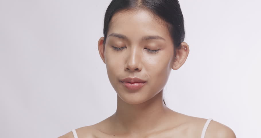 Close up portrait of beautiful Asian woman smiling with glowing clear skin. Charming model posing against white background for studio beauty shot.