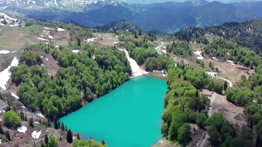 Green Lake recedes beneath descending aerial view across turquoise water, forest and snow-lined slopes in Adjara, Georgia, supporting alpine tourism, hiking promotion and remote destination media.