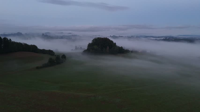 over a foggy valley with a wooded hill emerging from morning mist	