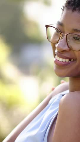 Vertical video: Pal smiling, woman leaning on pal shoulder in glasses and top at park, copy space. Outdoor, friendship, interaction, sunlit, softfocus, foliage, vertical video