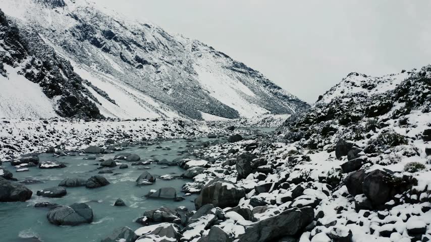 Snow covers the landscape as the river winds through rocky terrain and under steep mountain slopes in a cold environment of winter beauty
