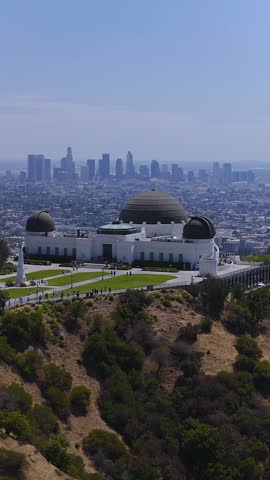 Aerial perspective looking over Griffith Observatory on Mount Hollywood with visitors walking around the grounds and the Los Angeles skyline visible beyond.