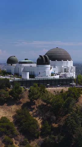 Aerial view moves towards the historic Griffith Observatory situated on the slopes of Mount Hollywood in Griffith Park, Los Angeles, on a bright sunny day.
