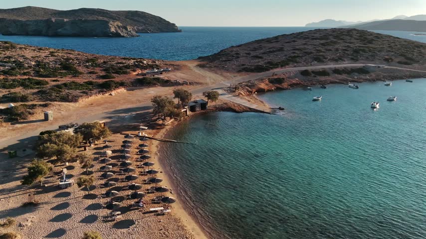 Aerial view of the double bay of Kalotaritissa beach with straw umbrellas and moored boats on Amorgos, Greece