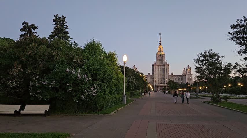 Evening view of university building, trees, benches, and walking people