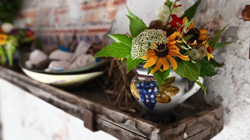 Historic Swiss farmhouse interior with wooden staircase, colorful flowers, brick wall and traditional household objects.