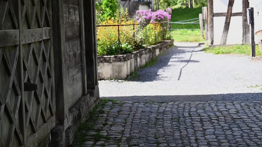 Historic timber-framed farmhouse with colorful flower garden and gravel path at Ballenberg Open Air Museum in Switzerland.