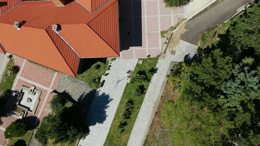 Direct overhead drone shot focusing on the main municipal building with red tiled roof in Belitsa town center, Bulgaria.