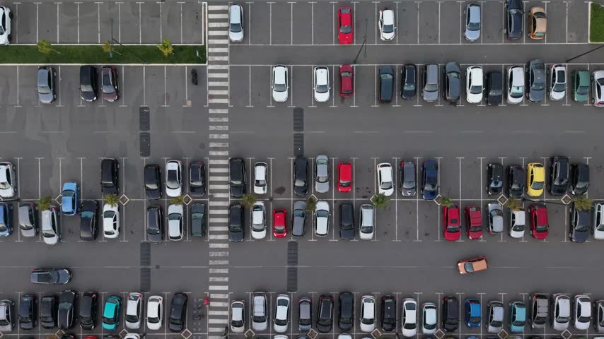 Many cars are parked in a large lot. Most spaces are occupied. People are walking between vehicles.