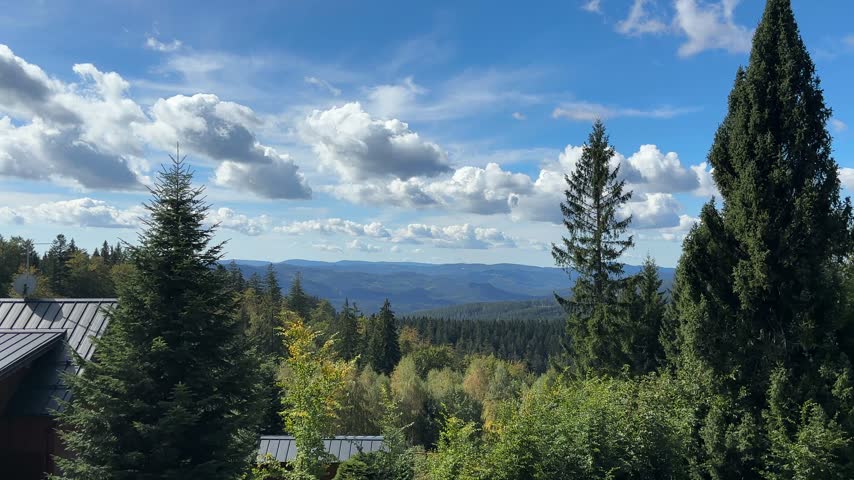 Scenic view of the Beskids mountain landscape with forested hills, green vegetation and distant mountains under a blue sky with dramatic clouds.
