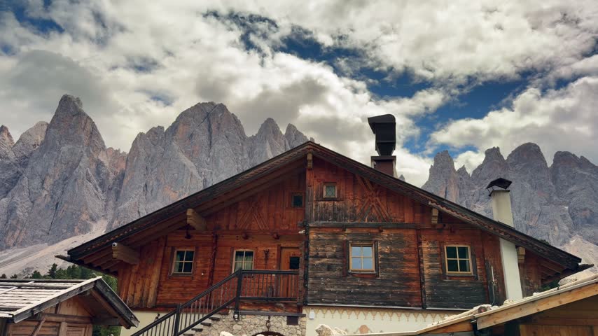 Traditional wooden alpine cabin surrounded by mountain landscape beneath moving clouds in the Dolomites, South Tyrol, Italy.
