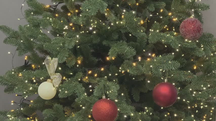 Close up of Christmas tree ornaments with red balls and glowing lights. Festive decoration detail. Perfect for holiday branding and seasonal visuals.