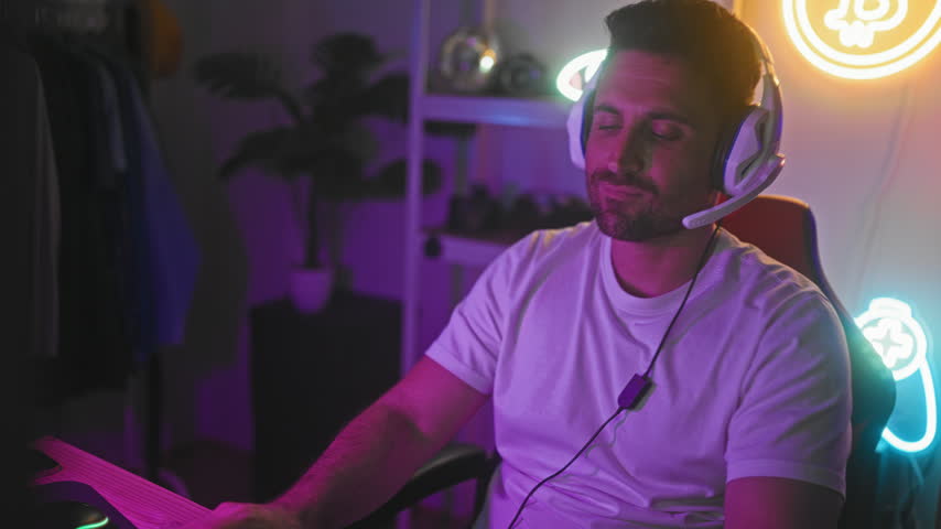 Man wearing gaming headset using computer in studio, hands on keyboard playing video game; concentration determination.