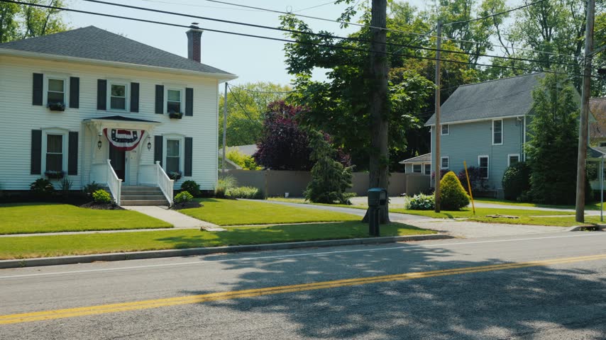Scenic view featuring two classic wooden residential houses situated side by side along peaceful neighborhood road during sunny summer day with clear blue sky and verdant trees background.