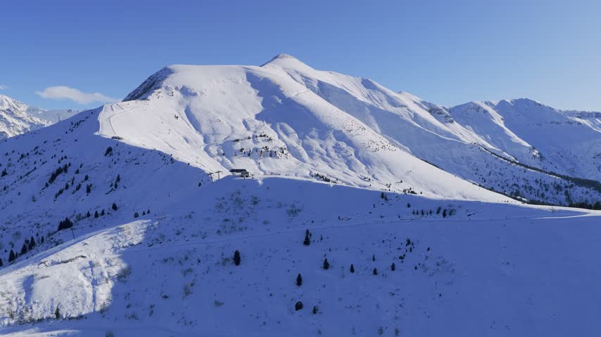 A sweeping aerial panorama of the French Alps in winter, featuring snow-covered mountains, forested slopes, and open alpine meadows. The scene includes views of Mont Blanc, Mont Joly, and the Megeve