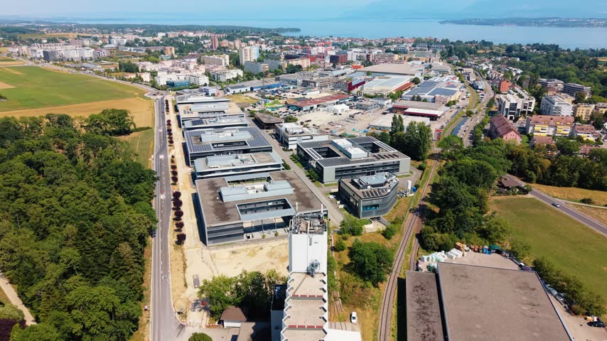 Flat rooftops top a business park near Nyon Switzerland, lake visible beyond, drone advancing