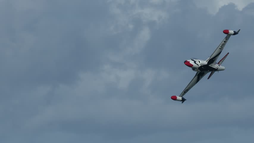 A vintage military jet performs a dynamic aerobatic maneuver against a clear blue sky.