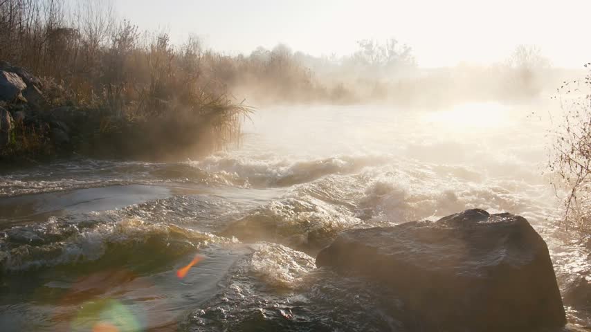 Misty morning river landscape with sun flare and flowing water over rocks