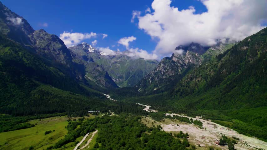 Winding glacial river streams through alpine meadows beneath towering jagged mountain peaks.