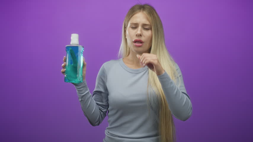 Woman holding a bottle of mouthwash, coughing into a fist and clutching her throat in studio; disgust.