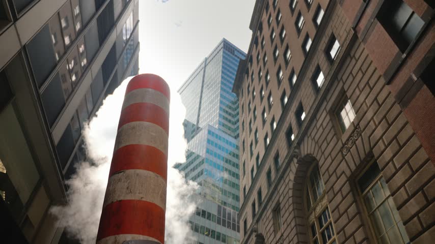 Low angle view of iconic NYC steam pipe blowing white smoke against modern skyscrapers in financial district, capturing urban steam system of Manhattan with dynamic cloud movement.