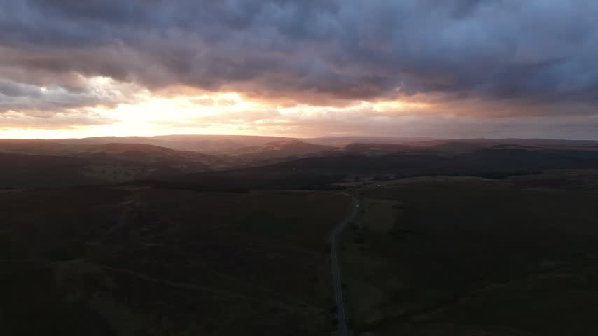 Sunset over the Hope Valley in the Peak District, England, with a scenic rural road winding through rolling hills and countryside beneath warm evening light.