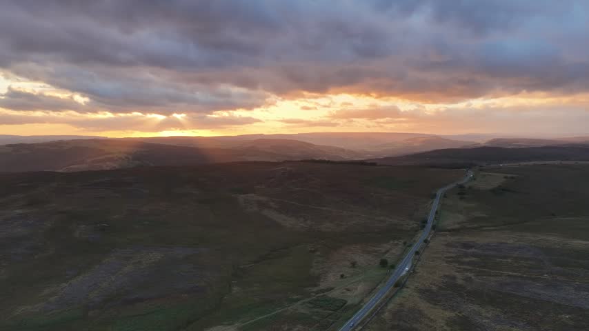 Sunset over the Hope Valley in the Peak District, England, with a scenic rural road winding through rolling hills and countryside beneath warm evening light.