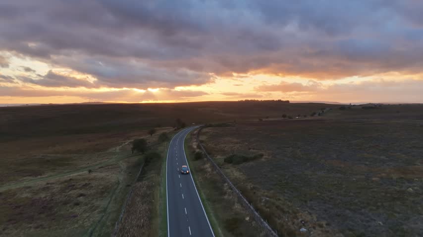 Sunset over the Hope Valley in the Peak District, England, with a scenic rural road winding through rolling hills and countryside beneath warm evening light.
