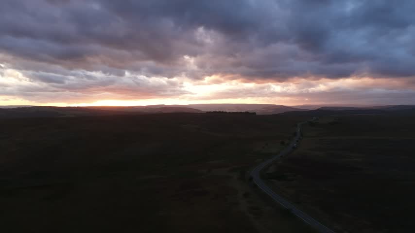 Sunset over the Hope Valley in the Peak District, England, with a scenic rural road winding through rolling hills and countryside beneath warm evening light.
