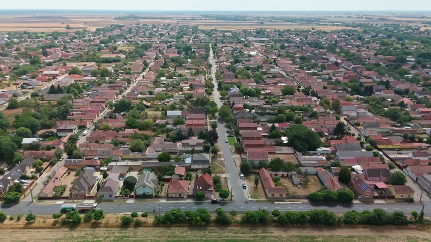 Hajdúböszörmény, Hungary cityscape with residential neighborhoods, streets, rooftops, trees and surrounding farmland under clear daytime skies in a wide aerial view.