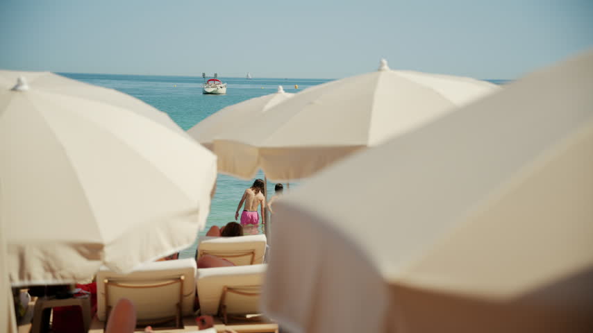 Soft focus shot of white beach umbrellas framing people relaxing near calm blue sea water