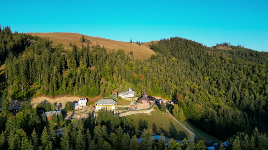 Orthodox monastery in Pojorâta, Bucovina, Romania, surrounded by the stunning Carpathian Mountains, forests and peaceful natural landscapes. Cinematic aerial view of sacred architecture.