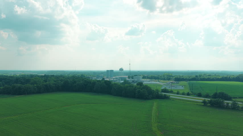 An industrial facility with storage towers, a water tower and an electrical substation sits isolated among green cropland and woodland, Xenia, Ohio, USA
