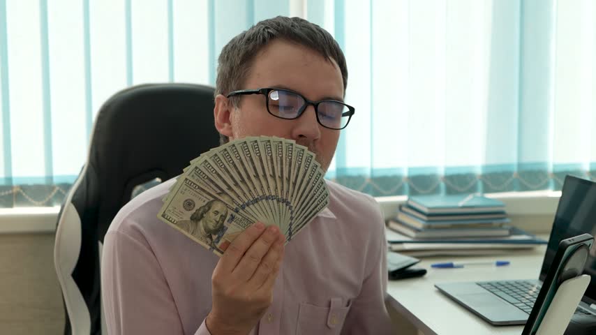 Businessman holding fan of hundred-dollar bills and smelling money. High profit, salary, and financial success in cash.