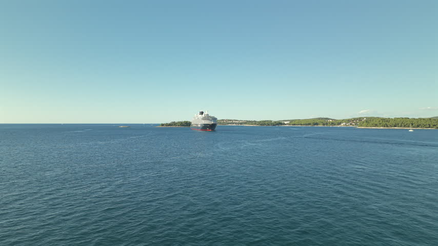 High angle view over calm blue Adriatic waters showing a large cruise ship in the distance near a green forested coastline under a clear sky