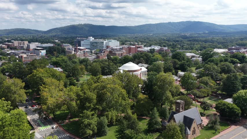 The stone tower of University Chapel overlooks leafy UVA grounds in Charlottesville, Virginia, with the Rotunda dome and columned facade beyond. Aerial view